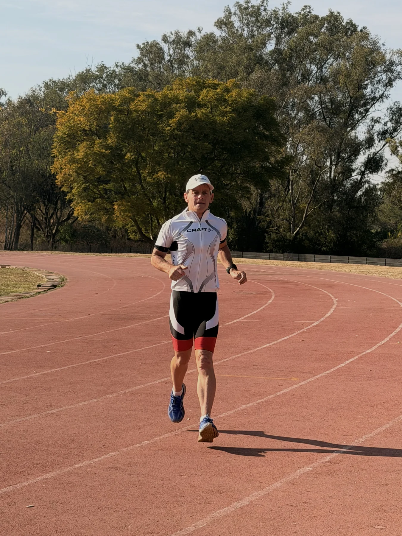 A runner in white training kit on an outdoor athletics track