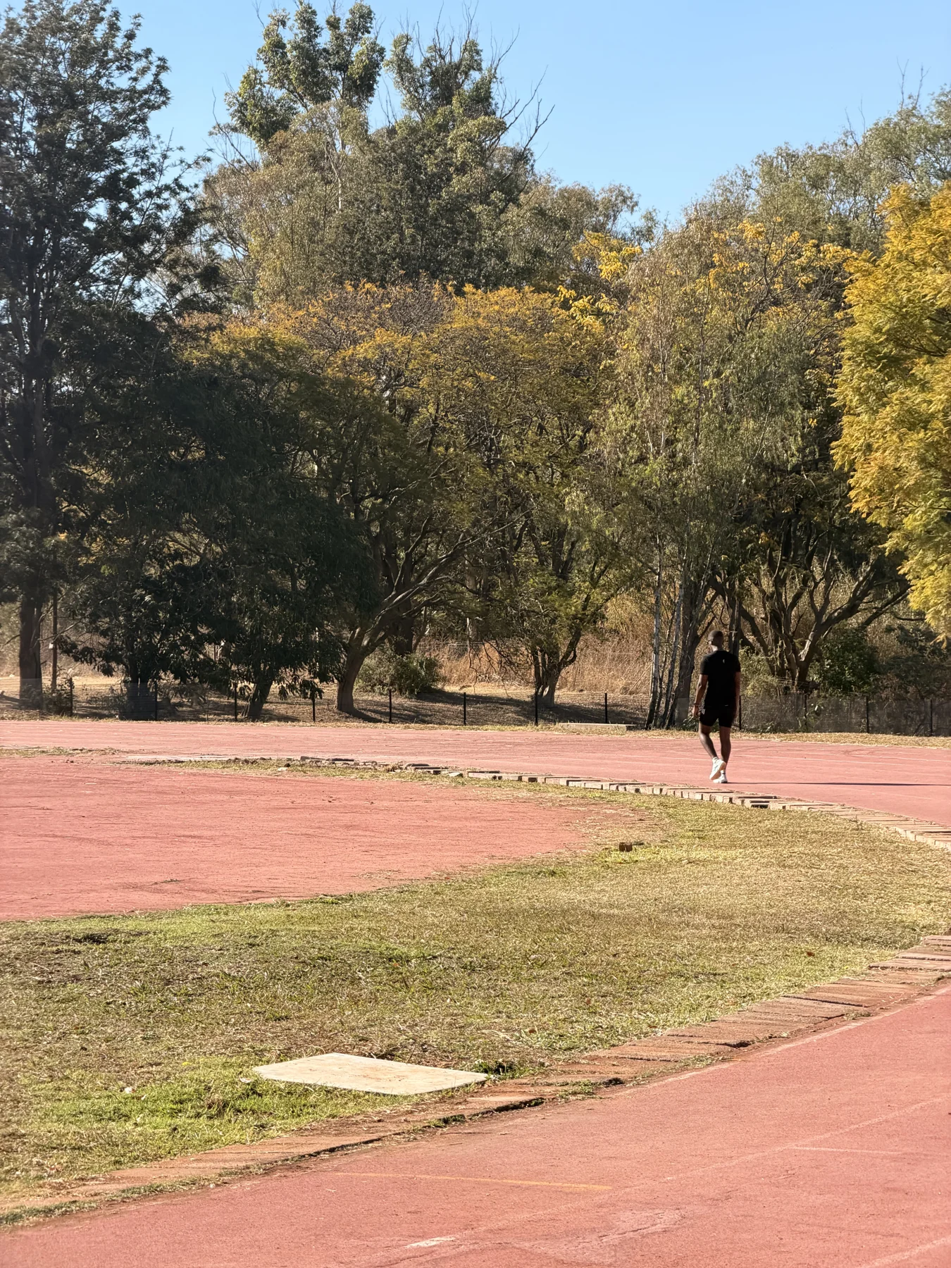 An athlete walking along an outdoor track surrounded by trees