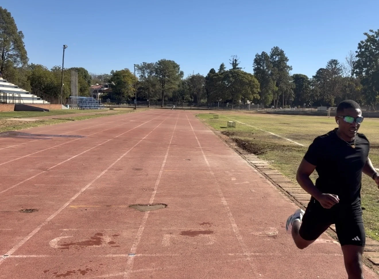 A runner in black training kit and sunglasses on an athletics track
